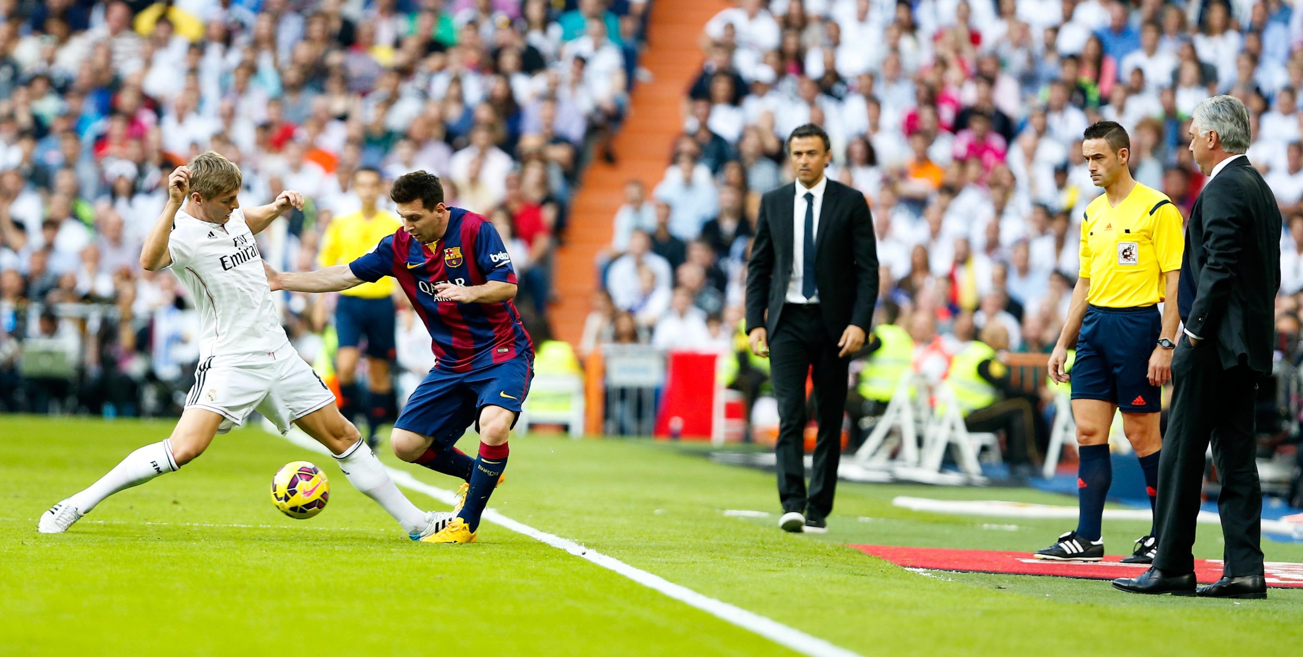 Luis Enrique observant Lionel Messi dribbler un joueur du Real Madrid lors d'un Clasico.