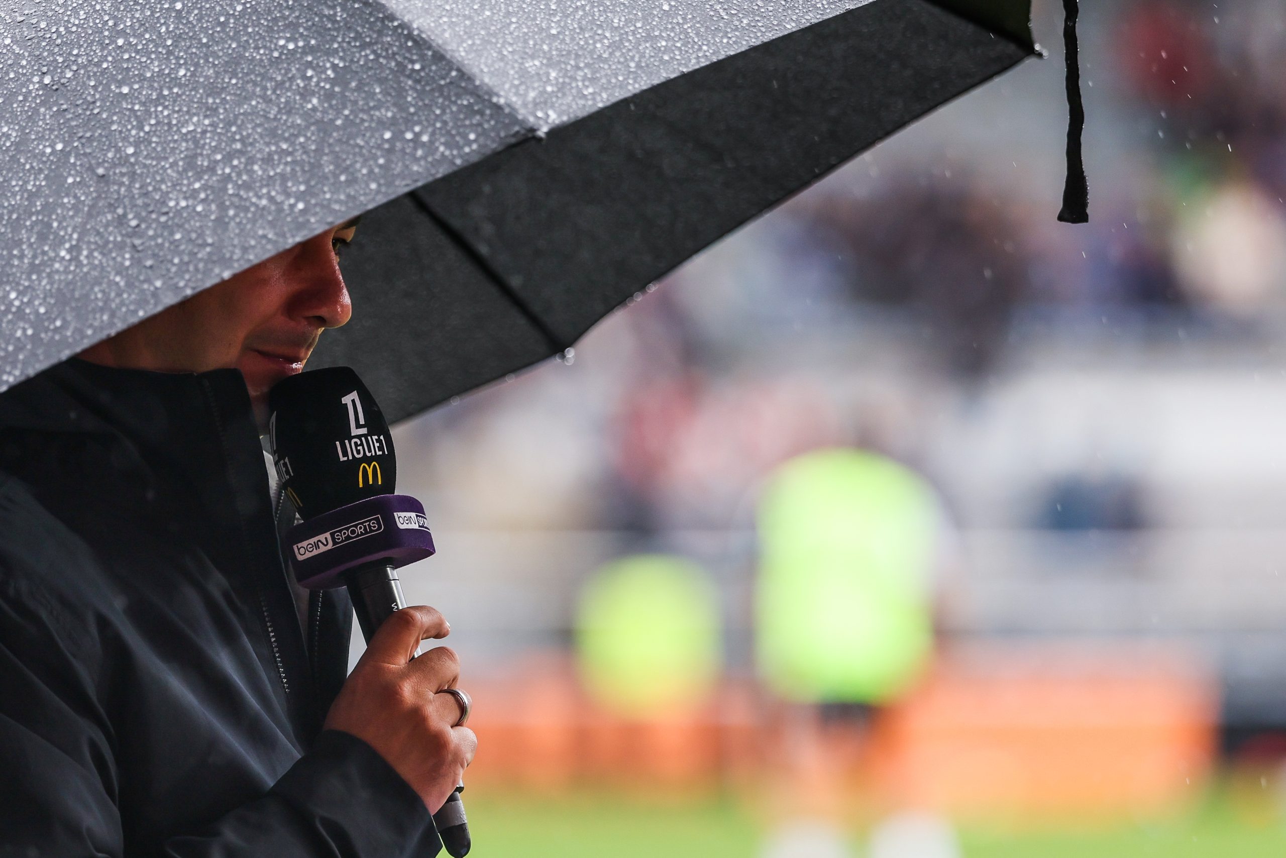 Un journaliste de beIN s'abritant sous un parapluie lors d'une rencontre de Ligue 1.