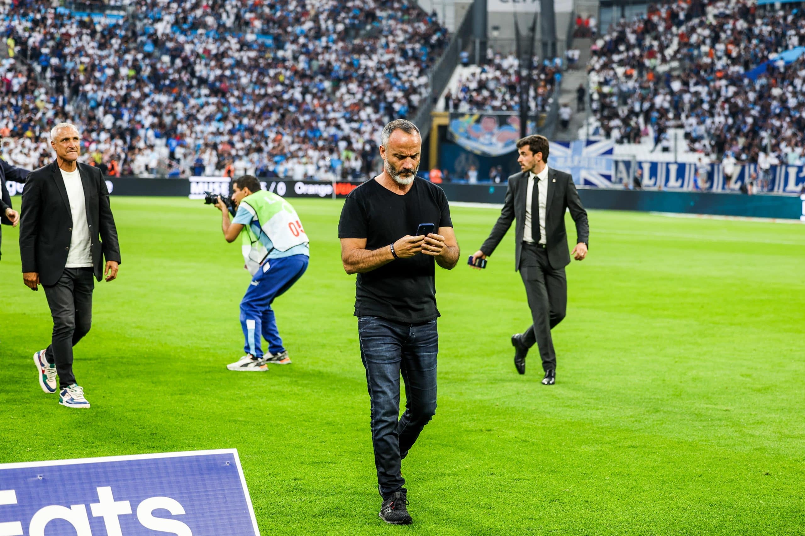 Eric Di Méco regardant son téléphone sur la pelouse du Vélodrome.